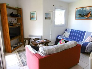 Ein Wohnzimmer mit einem roten Sofa, einem blau gestreiften Schlafsofa, einem Holzbücherregal, einem kleinen Tisch und einer Stehlampe.