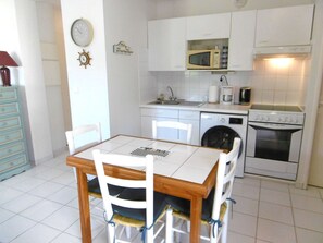 Eine Küche mit weißen Schränken, einer Mikrowelle, einer Kaffeemaschine, einem Geschirrspüler und einem Backofen. Ein Esstisch mit Stühlen ist ebenfalls vorhanden.