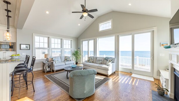 A spacious living area with a large window, a ceiling fan, and a fireplace. - Popponesset-Exclusive Oceanfront Rental, 3 bedroom, 3.5 baths, sleeps 6 (Mashpee)
