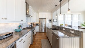 A modern kitchen with white cabinetry, stainless steel appliances, granite countertops, and pendant lighting. - Popponesset-Exclusive Oceanfront Rental, 3 bedroom, 3.5 baths, sleeps 6 (Mashpee)