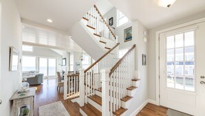 A spacious living area with a wooden staircase, a large window, and a view of the outdoors. - Popponesset-Exclusive Oceanfront Rental, 3 bedroom, 3.5 baths, sleeps 6 (Mashpee)