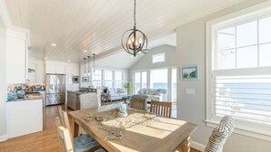A spacious kitchen with a central island, a dining area with a wooden table, and large windows offering a view of the ocean. - Popponesset-Exclusive Oceanfront Rental, 3 bedroom, 3.5 baths, sleeps 6 (Mashpee)