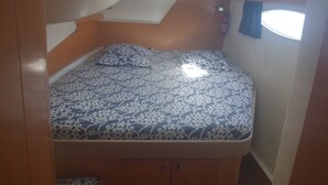 A small, enclosed sleeping area with a patterned bedspread, a headboard, and a window with curtains.