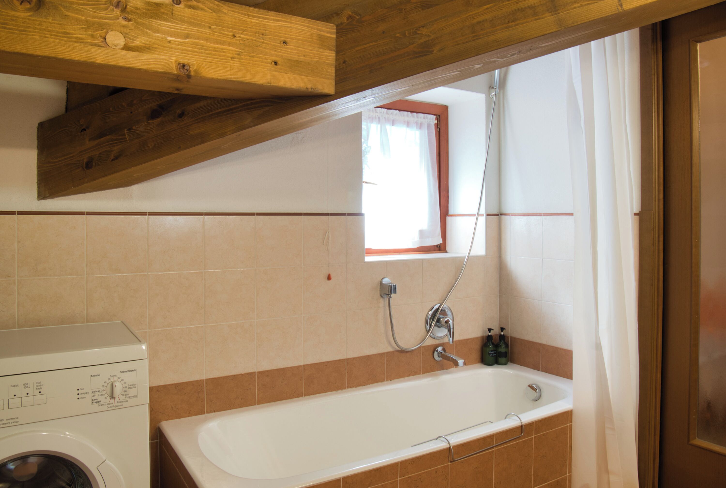 A bathroom with a washing machine, a bathtub, and a window with curtains.