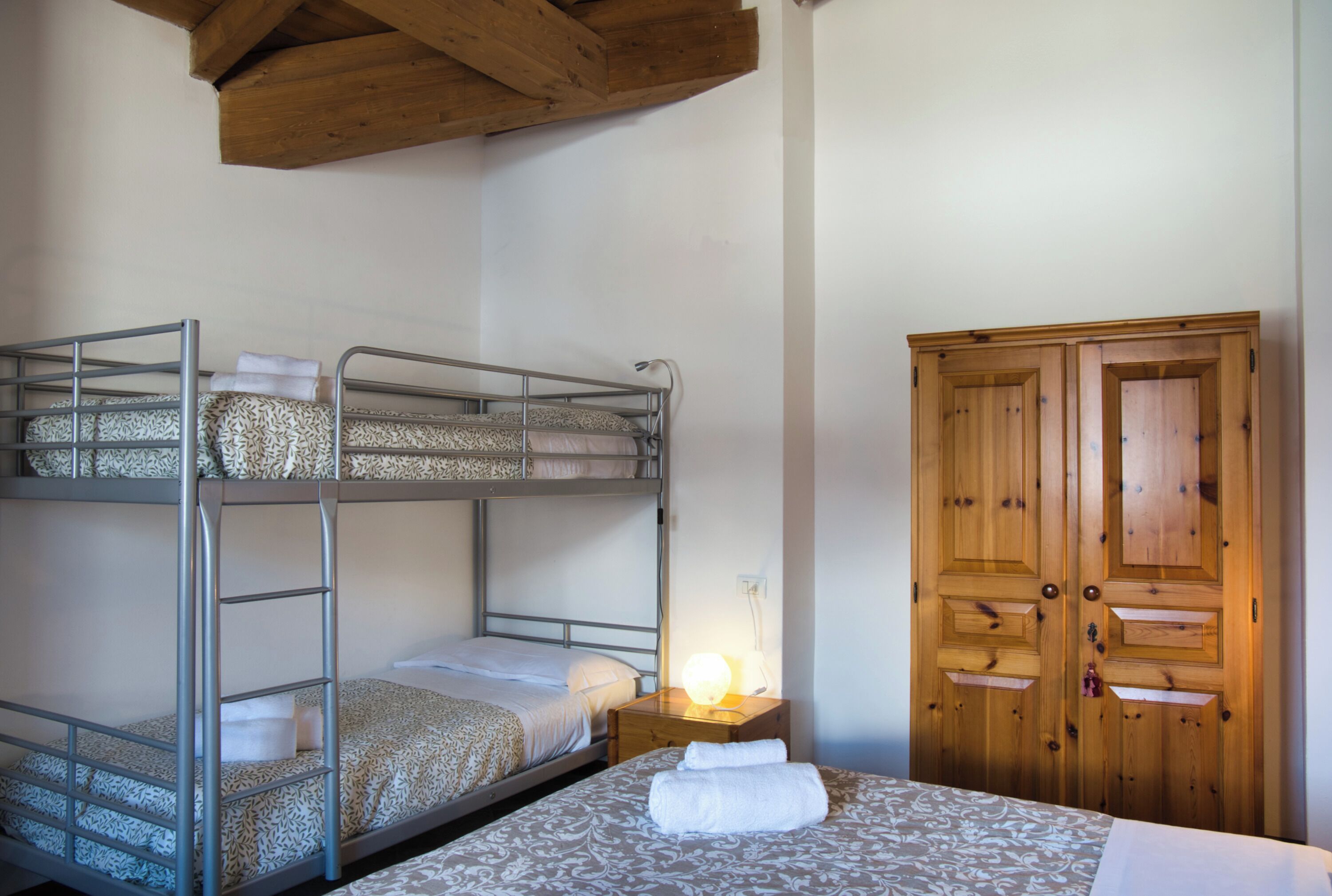 A bunk bed room with a wooden wardrobe and a bedside lamp.