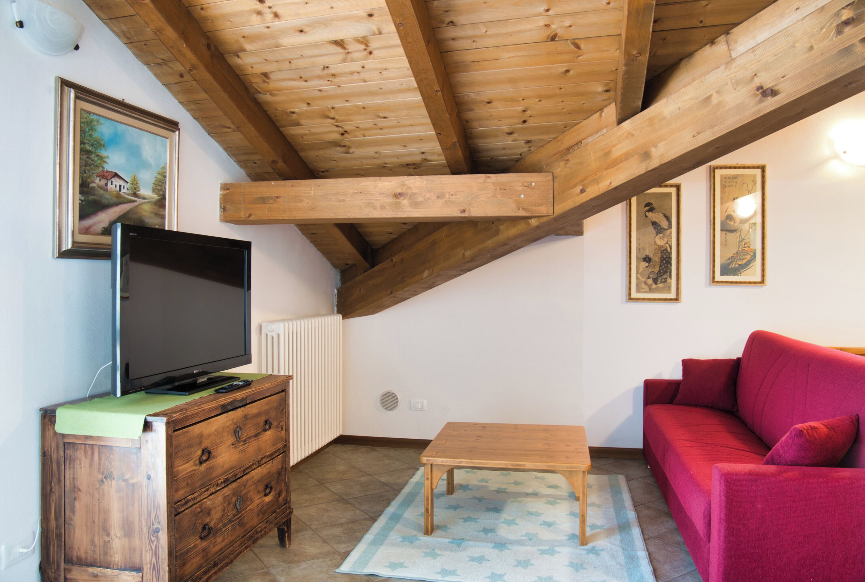 A room with a wooden ceiling, a television on a wooden cabinet, a red sofa, and a small wooden table.
