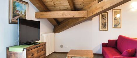 A room with a wooden ceiling, a television on a wooden cabinet, a red sofa, and a small wooden table.
