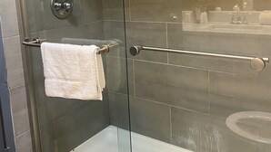 Eine Duschkabine mit Glastüren, ein weißes Handtuch, eine Handbrause und eine sichtbare Toilette im angrenzenden Raum.