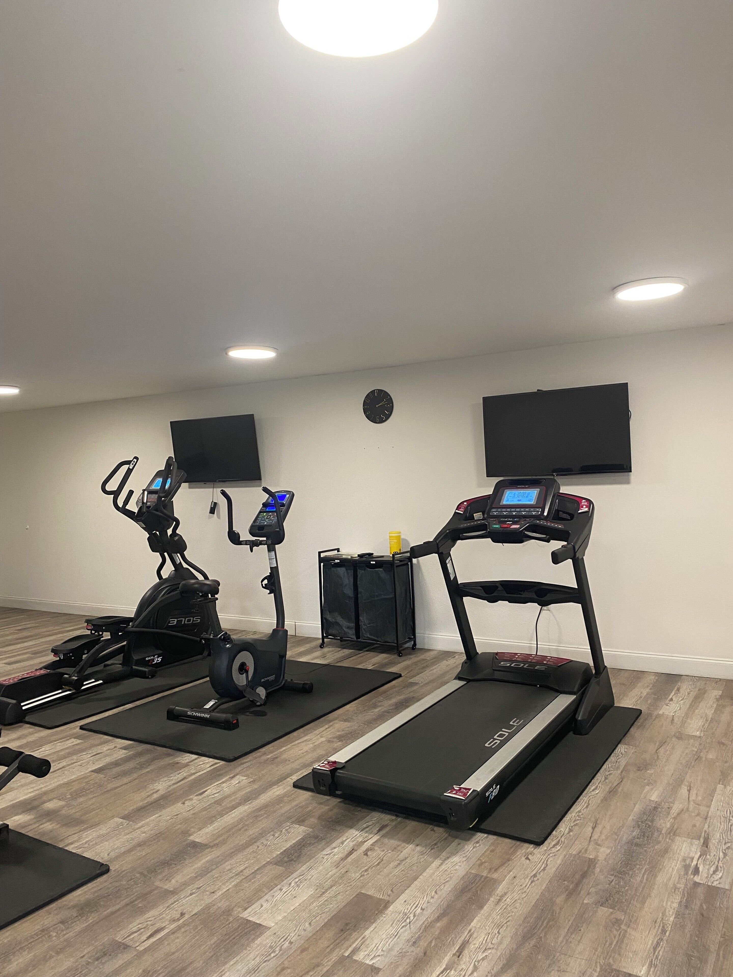 Une salle de sport à domicile équipée de deux tapis de course, d’un vélo d’appartement et d’un banc de musculation.