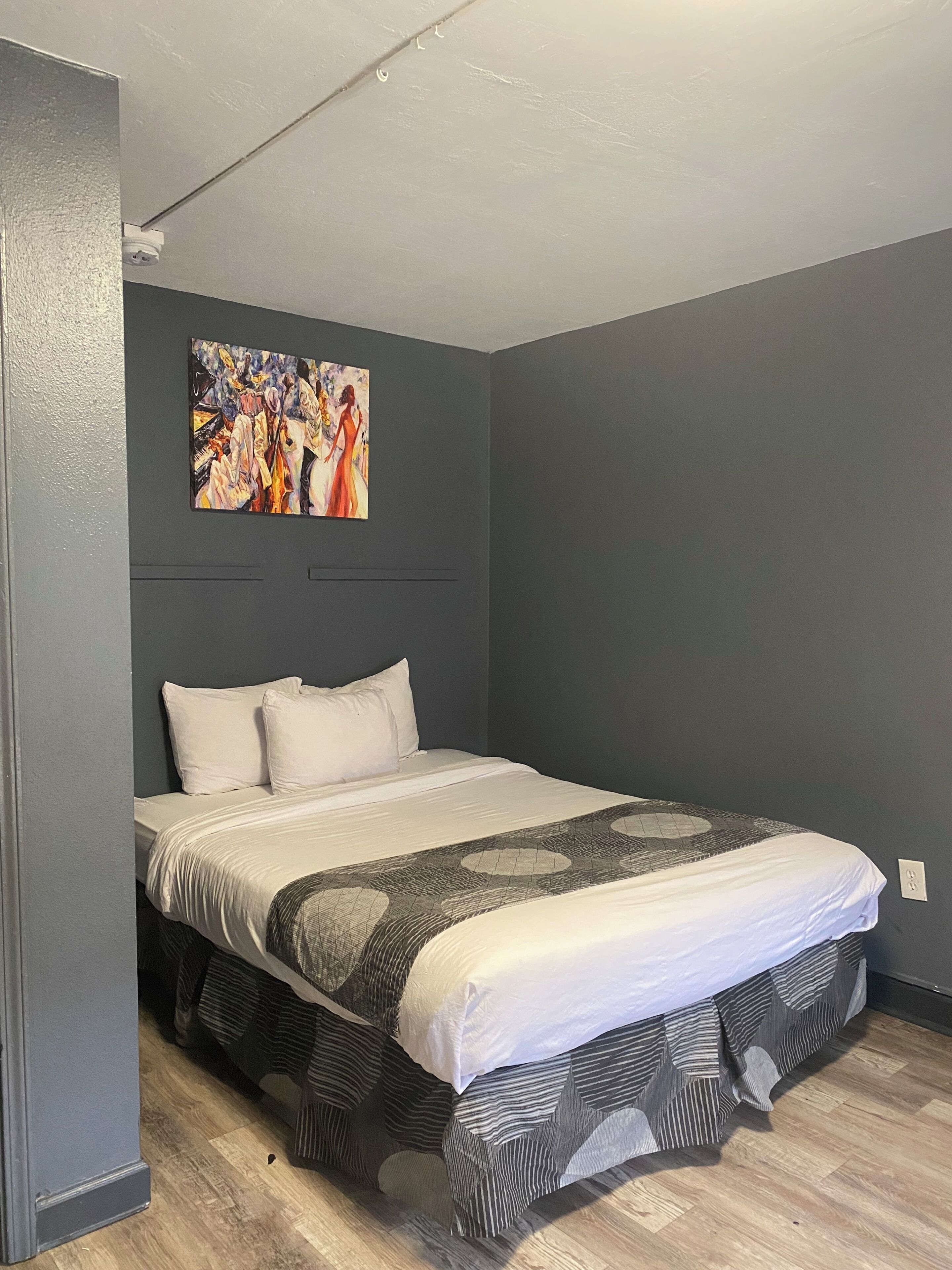 A bedroom with a bed, a painting on the wall, and a ceiling light.