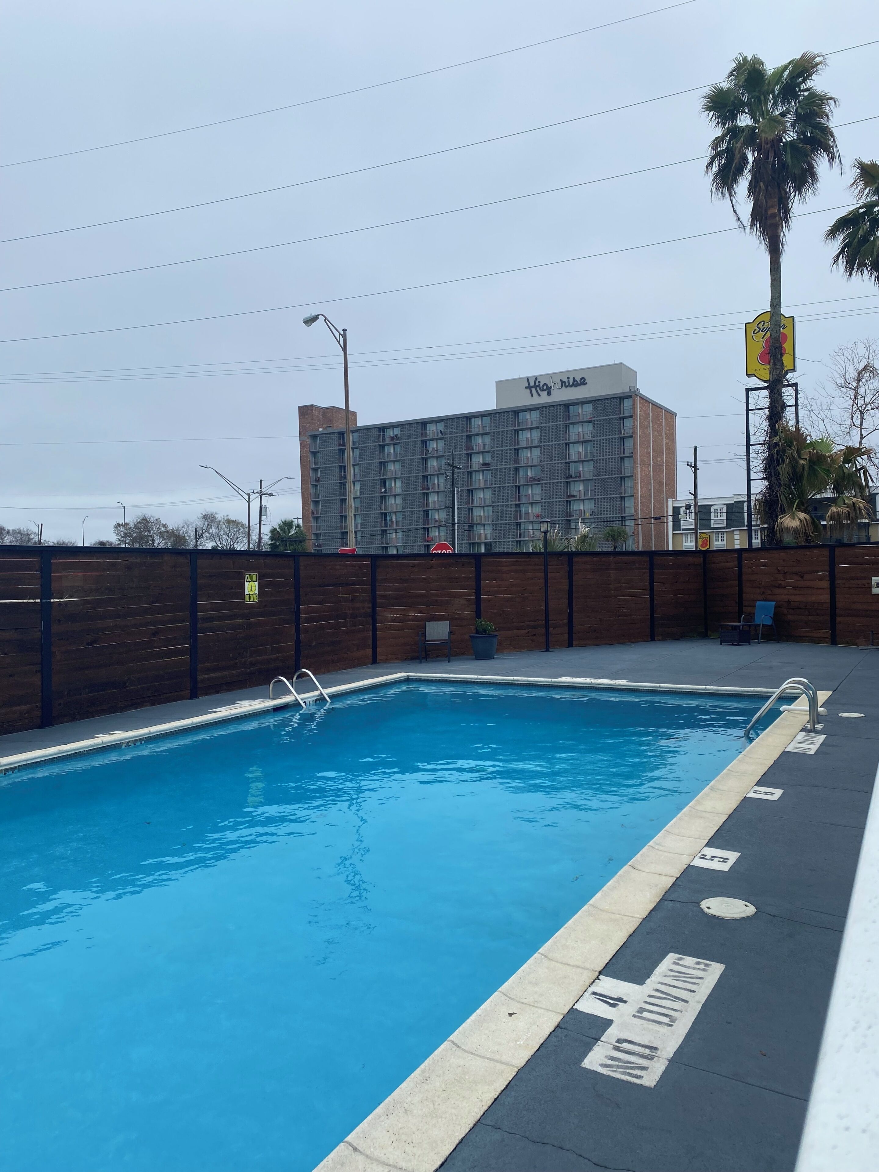 Une piscine entourée d’une clôture en bois, un panneau de signalisation et, au fond, un immeuble d’habitation.