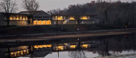 A multi-story house with a visible staircase, a dock extending into a body of water, and a reflection of the house in the water.
