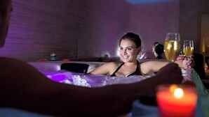 Une personne dans un bain à remous, avec une bougie et deux coupes de champagne.