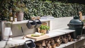 Een moderne buitenkeuken met een ingebouwde bank, een barbecue en diverse kookgerei en ingrediënten.