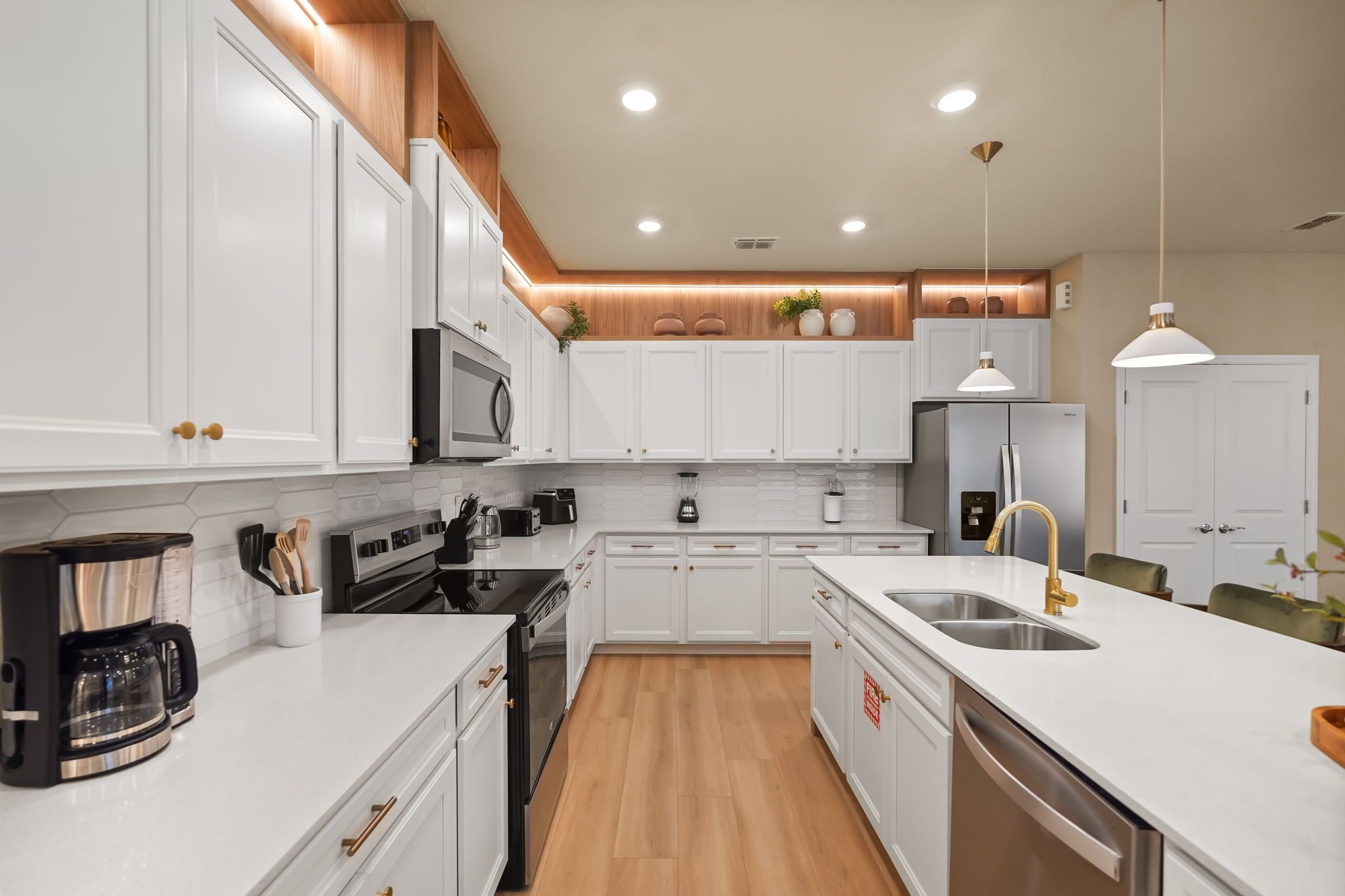 A modern kitchen with white cabinetry, stainless steel appliances, and a wooden floor.