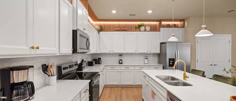 A modern kitchen with white cabinetry, stainless steel appliances, and a wooden floor.