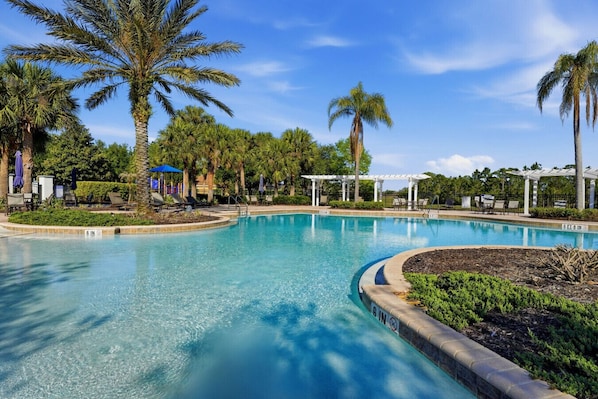 Ein Swimmingpool mit Liegestühlen und Sonnenschirmen, umgeben von Palmen und einer Pergola.