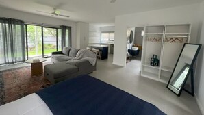 A modern hotel room with a large bed, a seating area with a sofa and armchair, a desk, and a walk-in closet. - Guestwick by the Sea Private cosy unit walking distance to beach, shops (Dromana)