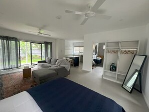 A modern hotel room with a large bed, a seating area with a sofa and armchair, a desk, and a walk-in closet. - Guestwick by the Sea Private cosy unit walking distance to beach, shops (Dromana)