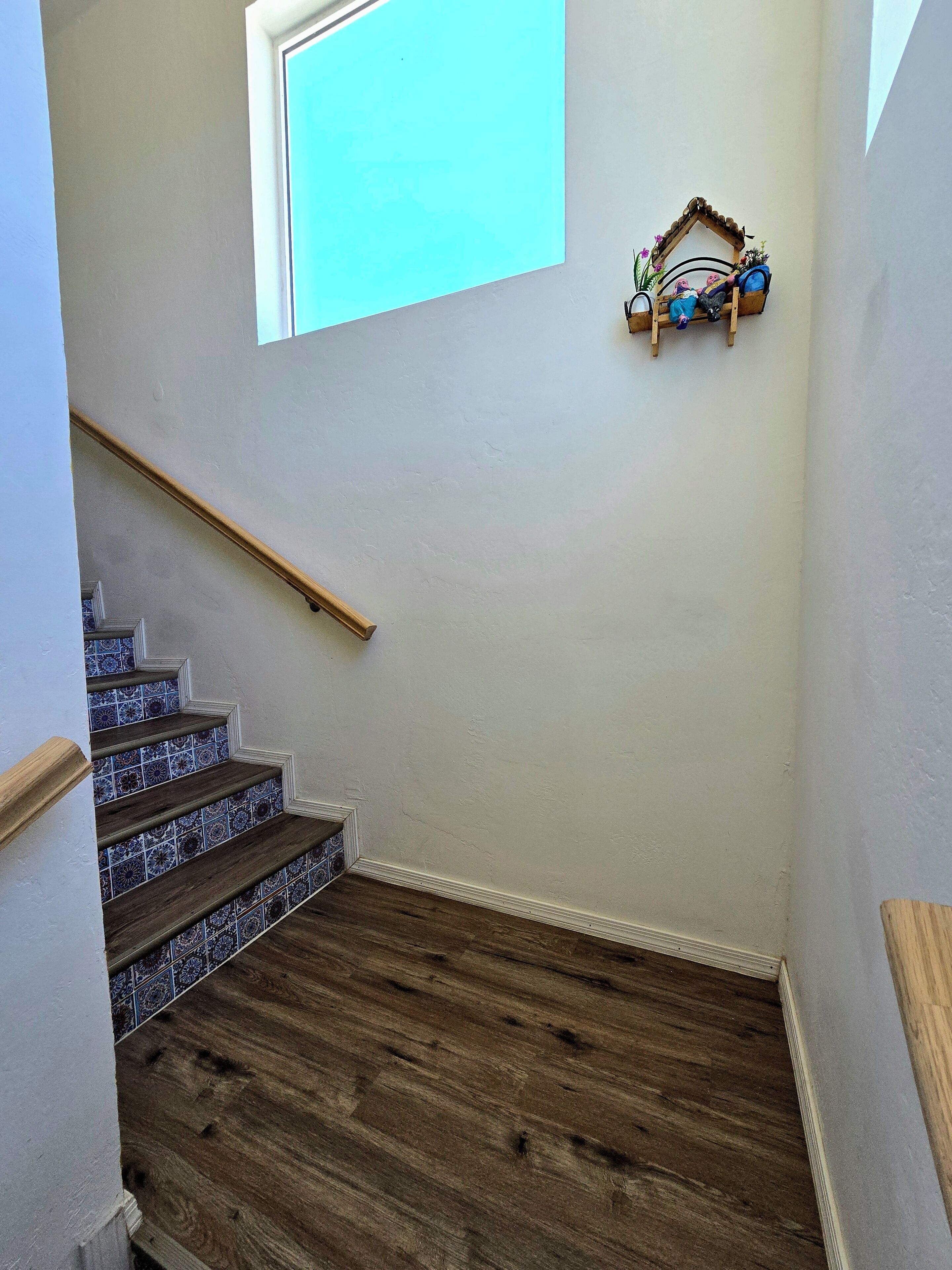 Una escalera con escalones de madera y azulejos azules con diseño, una barandilla de madera y un pequeño estante con adornos.