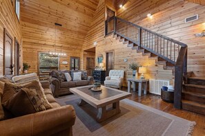 Ein Holzblockhaus-Interieur mit Treppe, Holzwänden, einer Couch, einem Sessel und einem Couchtisch.