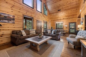 Ein Blockhaus-Interieur mit Kamin, zwei Sofas, einem Couchtisch und einem Essbereich.