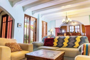 A living room with a sofa, armchair, and coffee table, a chandelier, and a view of a kitchen through an open door. - AV78 | Mountain Views | Community Pool | Rooftop Tower! (Loreto)