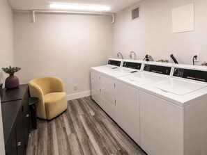A laundry room with three white commercial washers and dryers, a yellow chair, and a potted plant. - Central DC Studio w. Coffee In-unit  & AC (Washington)