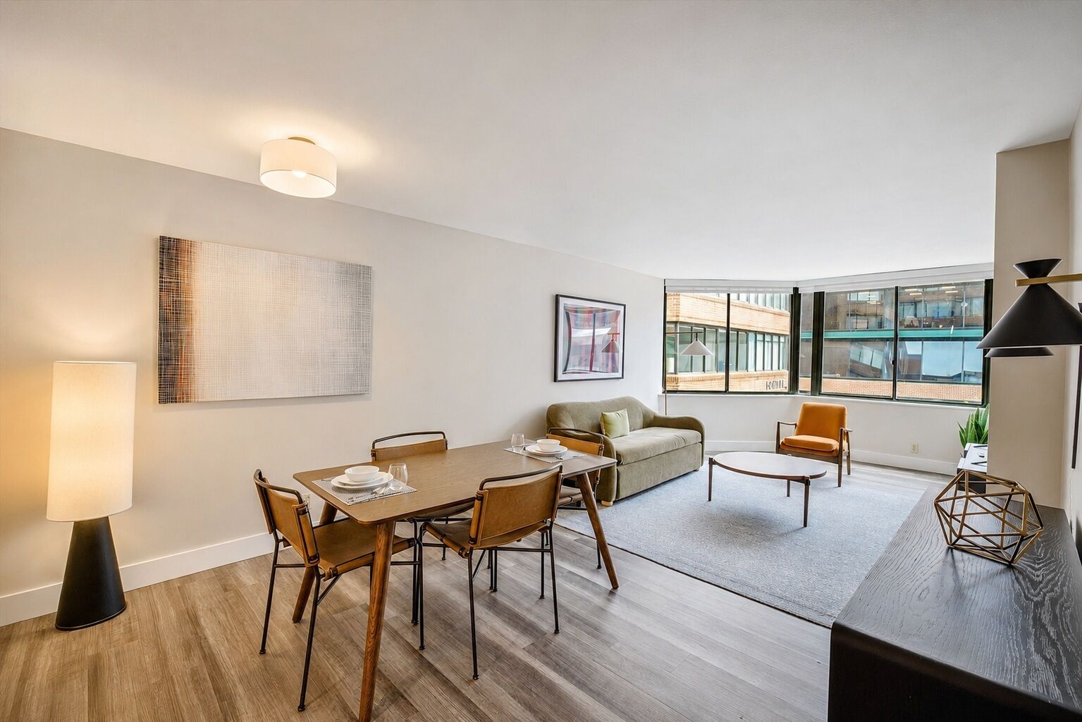 A modern living room with a dining table, sofas, and a large window offering a view of the city.