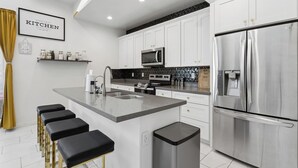 Una cucina moderna con mobili bianchi, elettrodomestici in acciaio inossidabile, un'isola centrale con sgabelli da bar e un forno a microonde sopra il piano cottura.