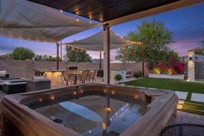 Eine Terrasss mit Whirlpool, Grill und Essbereich unter einer Markise.