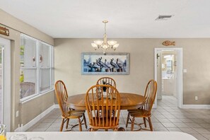 A dining area with a round table, wooden chairs, a chandelier, and a painting on the wall. - Tropical Backyard Oasis in Cocoa Beach | Heated Pool, BBQ Grill & Fire Pit ☀️ (Cocoa Beach)