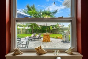 A view through a window of a patio area with outdoor furniture, a grill, and a decorative umbrella. - Tropical Backyard Oasis in Cocoa Beach | Heated Pool, BBQ Grill & Fire Pit ☀️ (Cocoa Beach)