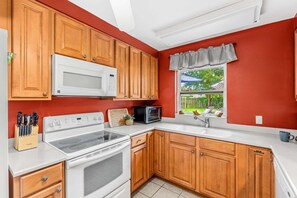 A kitchen with wooden cabinets, a white stove, a microwave, and a toaster. - Tropical Backyard Oasis in Cocoa Beach | Heated Pool, BBQ Grill & Fire Pit ☀️ (Cocoa Beach)