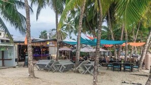 Ett område vid stranden med palmer, utomhusservering och en bar.