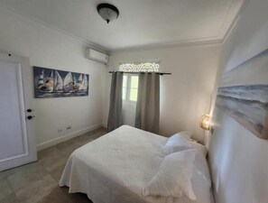 Ein Schlafzimmer mit einem Bett, einem Segelboot-Gemälde, einer Deckenleuchte und einem Fenster mit Vorhängen.