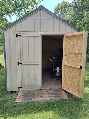 A small wooden shed with a door open, revealing a propane tank inside.