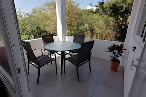 Ένα μπαλκόνι με ένα στρογγυλό τραπέζι και τέσσερις καρέκλες, ένα φυτό σε γλάστρα και έναν λευκό τοίχο.
