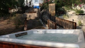 Ett bubbelbad i en trädgård med ett staket av trä, en stenmur och några växter.