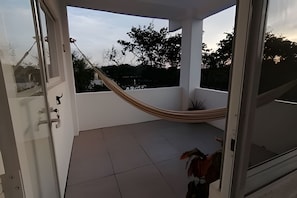 Un balcon avec un hamac, une plante en pot et une vue sur les arbres et les bĂątiments.