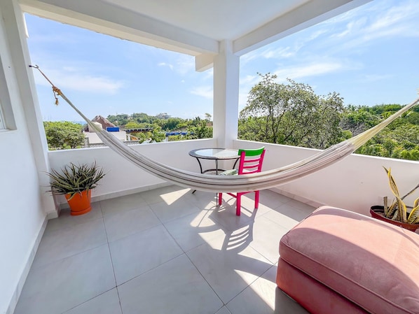 Ein Balkon mit einer Hängematte, einem Tisch, Stühlen und Topfpflanzen.