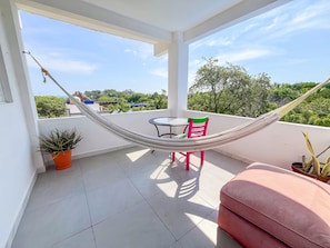 Un balcon avec un hamac, une table, des chaises et des plantes en pot.