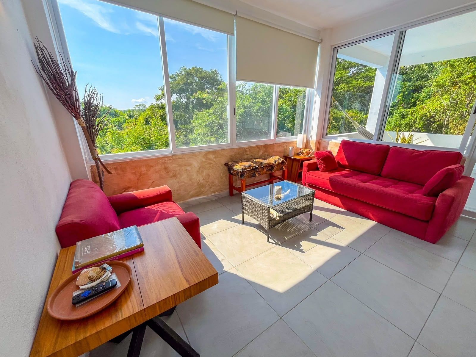 A sunlit room with a red sofa, a wooden coffee table, and a view of greenery outside.