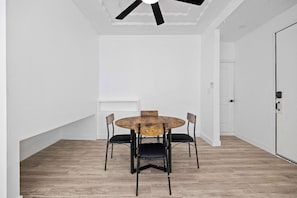 Ein Zimmer mit einem runden Holztisch, vier schwarzen Stühlen, einem Deckenventilator und einer weißen Tür.