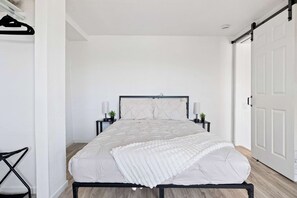 Ein Schlafzimmer mit einem Bett, Nachttischen, einer Hängelampe und einer Tür.