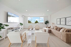 Ein modernes Wohnzimmer mit einer Couch, Sesseln, einem Couchtisch und einem an der Wand montierten Fernseher.