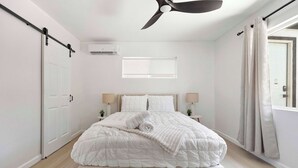 Ein Schlafzimmer mit Bett, Deckenventilator, Klimaanlage, Fenster und Vorhängen.