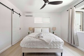Ein Schlafzimmer mit Bett, Deckenventilator, Klimaanlage, Fenster und Vorhängen.