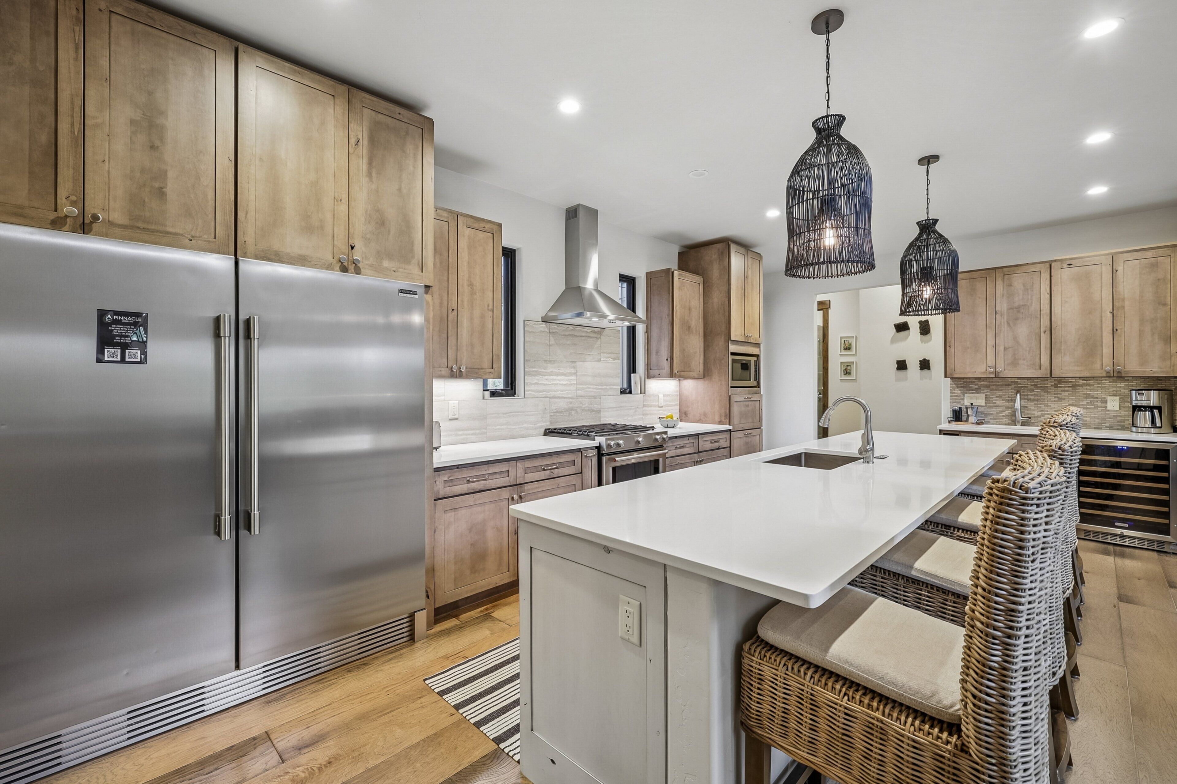 Une cuisine moderne avec des meubles en bois, des appareils en acier inoxydable, un îlot central, des chaises en osier et des luminaires suspendus.