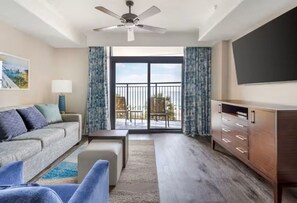 Ein modernes Wohnzimmer mit Sofa, Hocker und TV-Schrank, ein Balkon mit Blick und einem Deckenventilator.